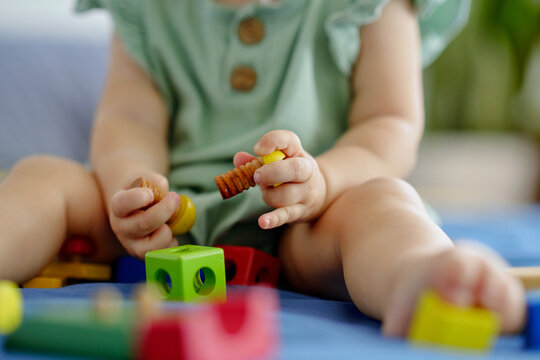 Closeup image of baby girl sitting on bed and playing with wooden blocks