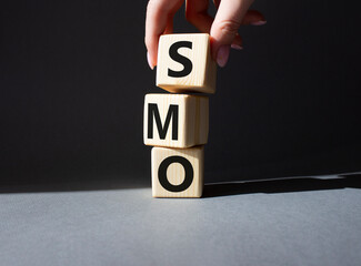 SMO - Social Media Optimization symbol. Wooden blocks with words SMO. Businessman hand. Beautiful grey background. Business and SMO concept. Copy space.