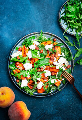 Grilled peach salad with feta cheese, hazelnuts and arugula on blue background, top view, copy space