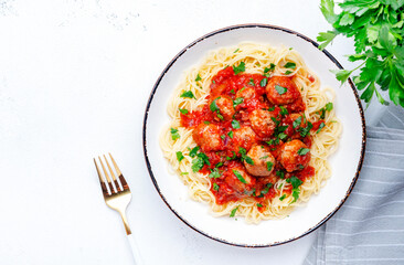 Spaghetti pasta with meatballs in spicy tomato sauce with parsley in plate, white table background, top view