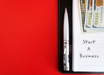 On copy space red background, notebook, money and pen with handwritten text START A BUSINESS,...