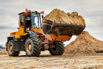Powerful wheel loader or bulldozer working on a quarry or construction site. Loader with a full bucket of sand. Powerful modern equipment for earthworks. - obrazy, fototapety, plakaty
