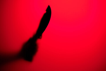 Hand holding large knife in red neon light.