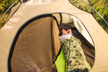 Happy girl rests in sleeping bag in tourist tent in nature.