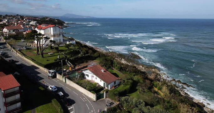 Drone flys over French Basque Country town Bidart with many basque homes along the coastline and Parlamentia surf break with waves crashing on the shore