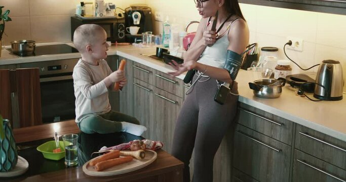 Young woman with a cardio monitor cooks lunch at home together with her three-year-old son