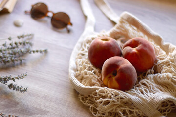 Mesh tote with fresh peacehs, lavender bouquet, round sunglasses, vintage book and seashell on the table. Selective focus.