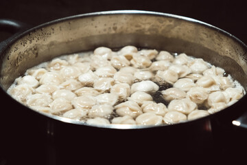 Small size meat dumplings are boiling in a pot on the stove. Pelmeni are the traditional national Russian cuisine. Italian ravioli. Food for children. Dish for kid. Cooking lunch or dinner for family