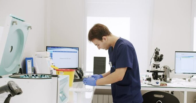 Handheld shot of male medical specialist in uniform preparing samples and using analyzing machine during work in lab of modern hospital.