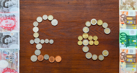 Euro and British Pound symbols made from coins, euro and pound paper banknotes next to it on wooden background. concept of mutual settlements of the EU countries and UK. Flat lay, mock up, top view