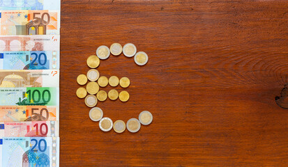  Euro symbol made of euro-cent coins and row of paper euro banknotes of different denominations on wooden background. Сoncept of finance and mutual settlements of countries of European Union