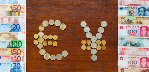 Euro and Yuan currency symbols made from coins on wooden background. Nearby there are paper Euro banknotes and Chinese Yuan money. Сoncept of international financial settlements. Flat lay, mockup