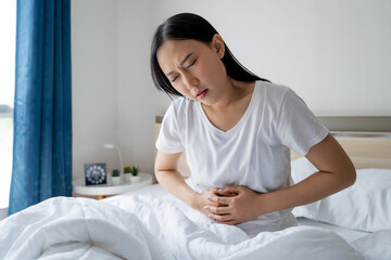 Obraz na płótnie Canvas Asian woman feeling sick and having stomachache while sitting in bed in the morning she felt a stomach ache or menstruation and abdominal pain