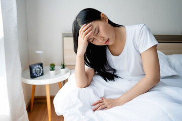 Asian woman feeling sick and having a headache maybe migraine while sitting in bed in the morning