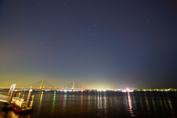 Fototapeta na wymiar 千葉県銚子市と茨城県神栖市に架かる銚子大橋の夜景と2月の星(カシオペア座,北極星等)を河岸公園から見る
