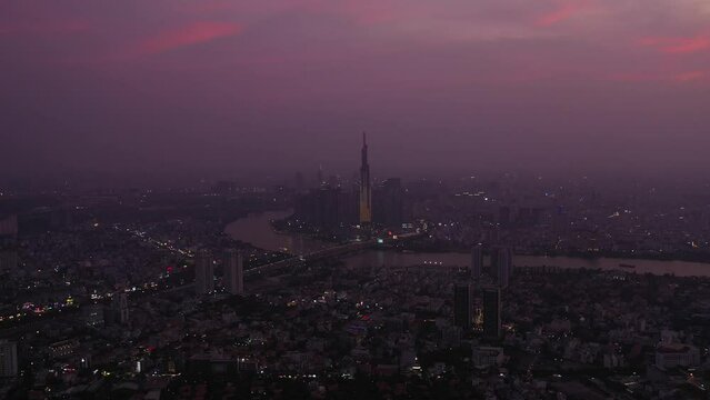 Aerial view of Ho Chi Minh City and Saigon river in the twilight with ambient and artificial light. Drone crane shot with camera rising into the air.
