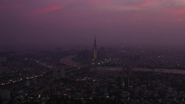 Aerial view of Ho Chi Minh City and Saigon river in the twilight with ambient and artificial light. Drone camera flies out to wider view.