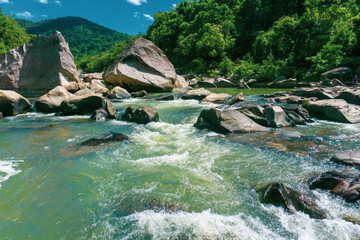 Tranquil natural scene with blue mountains, blue sky, and scattered rocks on the rippling river. Eco-tourism on a sunny day	