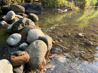 View of many rock pebble on the side of a river with beautiful water reflection.