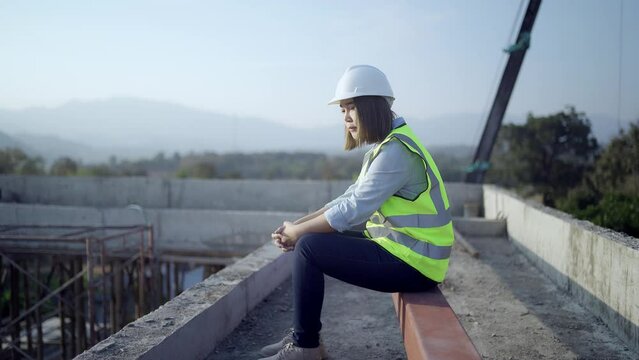Civil engineer woman sitting on Industrial building. Architect on construction site. Construction and architecture. Professional engineer in safety equipment. Reflective vest and hard hat