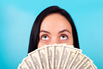 Portrait of shocked impressed girl hide face behind usd banknotes look up isolated on blue color background
