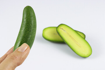 Close up of a hand holding mini avocado with a sliced cocktail avocado on the back isolated on white. Specially cultivated exotic green vegan food for healthy living. Functional food or a superfood