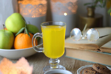 Cup of tea, plates with cookies, glass of orange juice, books, reading glasses, bowl of fruit and candles on the table. Selective focus.