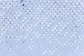 Black diamond shaped barbed wire after snow blizzard. Icy net covered by snow. Sow covered fence. Steel wire at snow day. Abstract pattern of white and black.