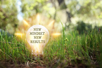 Hand holding light bulb with the text new mindset on the green grass - obrazy, fototapety, plakaty