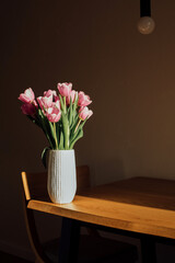 Gently pink bouquet of tulips in a white vase on wooden table. Spring background with a bouquet of flowers. Front view