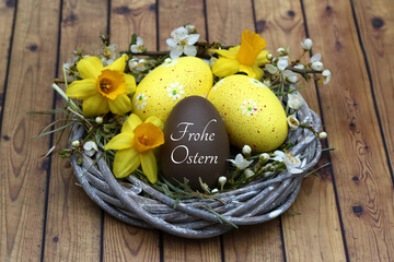 Osterei mit der Beschriftung Frohe Ostern in einem Nest dekoriert mit Narzissen.