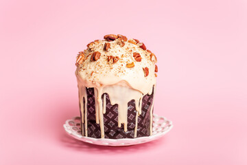 Tasty Easter cake decorated with white chocolate and pecan nuts on white round plate on pink background. Easter card.