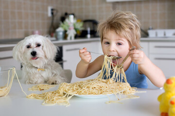 Little blond boy, toddler child, eating spaghetti for lunch and making a mess at home in kitchen