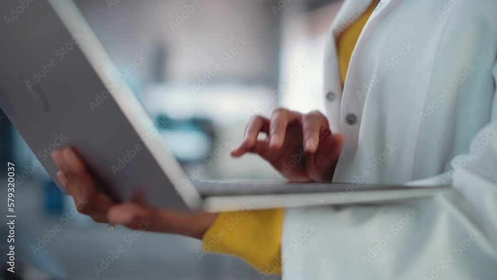 Poster close up on the hands of a black female in a lab coat using laptop computer, scrolling, and clicking