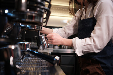 Close up of a barista preparing milk for coffee on a espresso machine in coffee shop.
