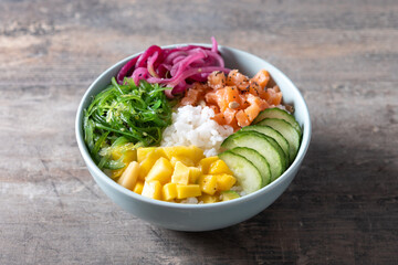Poke bowl with rice, salmon,cucumber,mango,onion,wakame salad, poppy seeds ands sunflowers seeds on wooden table