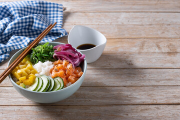 Poke bowl with rice, salmon,cucumber,mango,onion,wakame salad, poppy seeds ands sunflowers seeds on wooden table. Copy space
