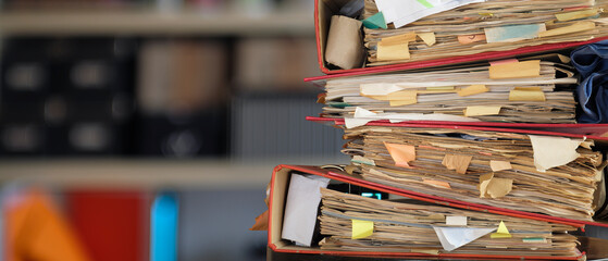 stack of dusty messy file folders, blurred office in the back,red tape,...