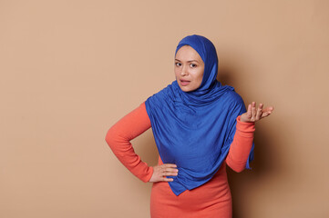 Beautiful middle-aged Muslim woman in stylish orange dress and blue hijab, expressing amazement...