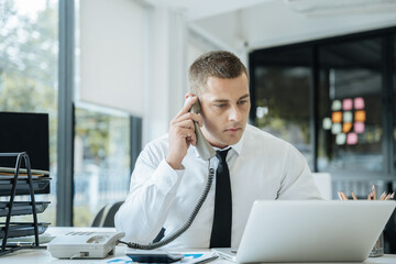 Obraz premium Businessman sitting in office using a cellphone and laptop.