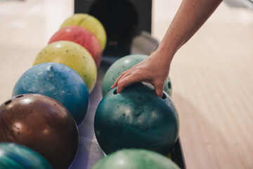 Close-up of a person's hand picking green bowling ball from rack