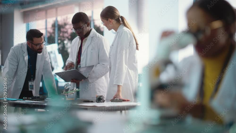 Poster Diverse Young Group of Engineers Working in a Startup Lab. Female Specialist Checking on Electronic Circuit Using Microscope While Team of Professionals Discuss Manufacturing Using Laptop Computer