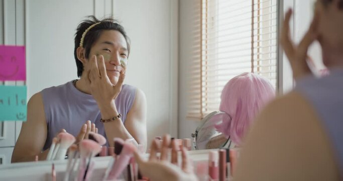 Gay queer man non-binary beauty blogger makeup artist at home cross dressing up apply face skin care eye make up brush. Real asia LGBT young guy adult people happy relax smile looking at mirror pride.
