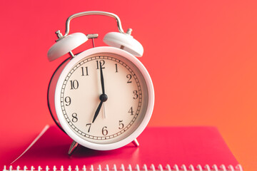 White alarm clock and notebook on Viva Magenta background.