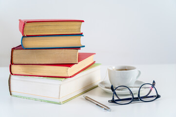 Stacks of books on a table, with a cup and glasses beside them. Study and culture.

