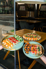 Sets of japanese sushi rolls with tuna, sea bass, salmon, cucumber, avocado, seaweed, cream cheese, mango, sesame in interior of restaurant.