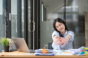 Asian businesswoman feel tired from hard work, thus doing arm stretching posture to relax body. Tired Asia woman stretching her hands while working in office.