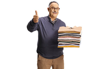 Cheerful mature man holding a pile of folded clothes and gesturing thumbs up
