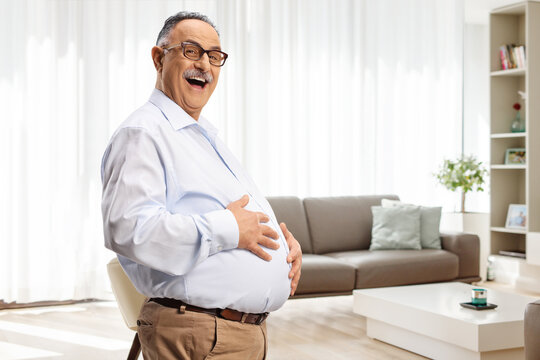 Mature man holding his big belly in a living room