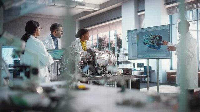 Diverse Professional Jet Engine Researchers Discussing Work, Using Laptop Computer and Checking Blueprints in Motor Manufacturing Facility. Scientists Developing Innovative Turbine Engine
